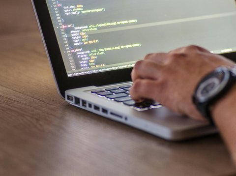 A close-up shot of a person coding on a laptop, focusing on the hands and screen.